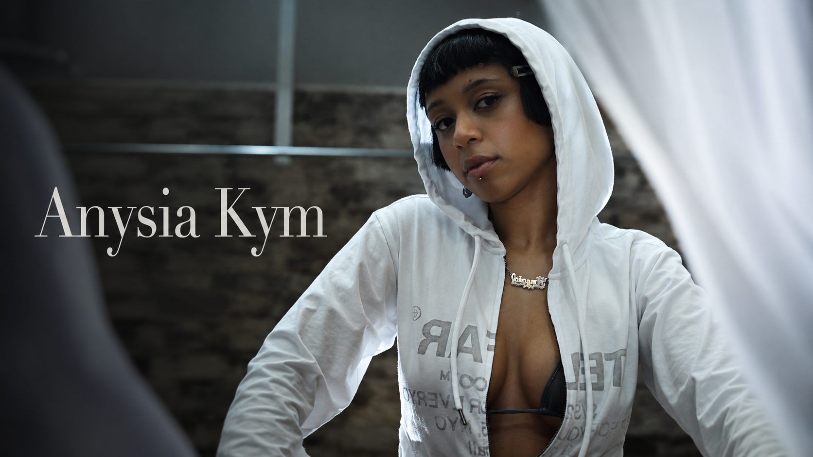 音樂人 Anysia Kym 穿白色連帽外套、站在室內的肖像