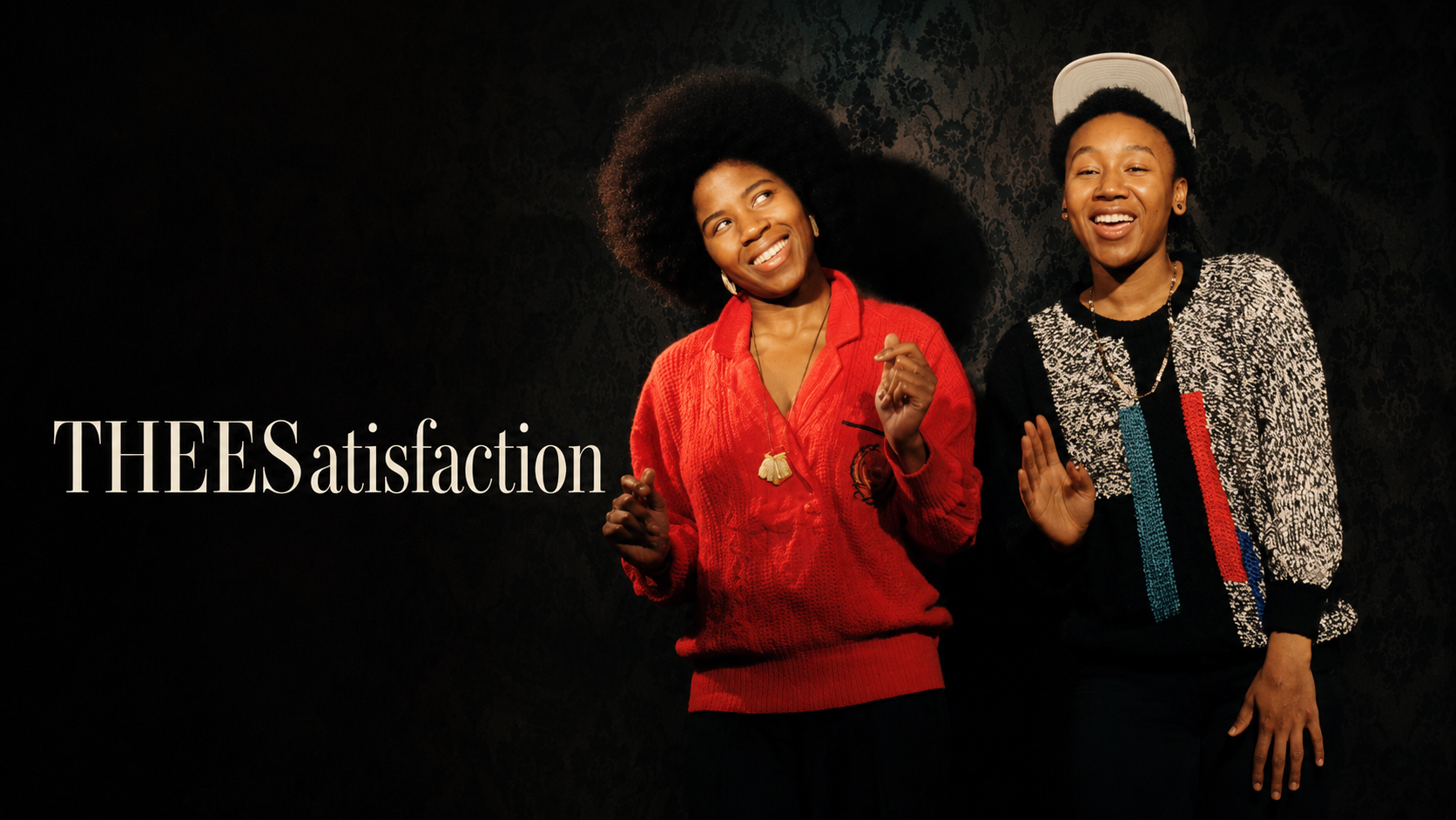 音樂組合 THEESatisfaction 的雙人肖像，兩人站在黑色花紋背景前微笑
