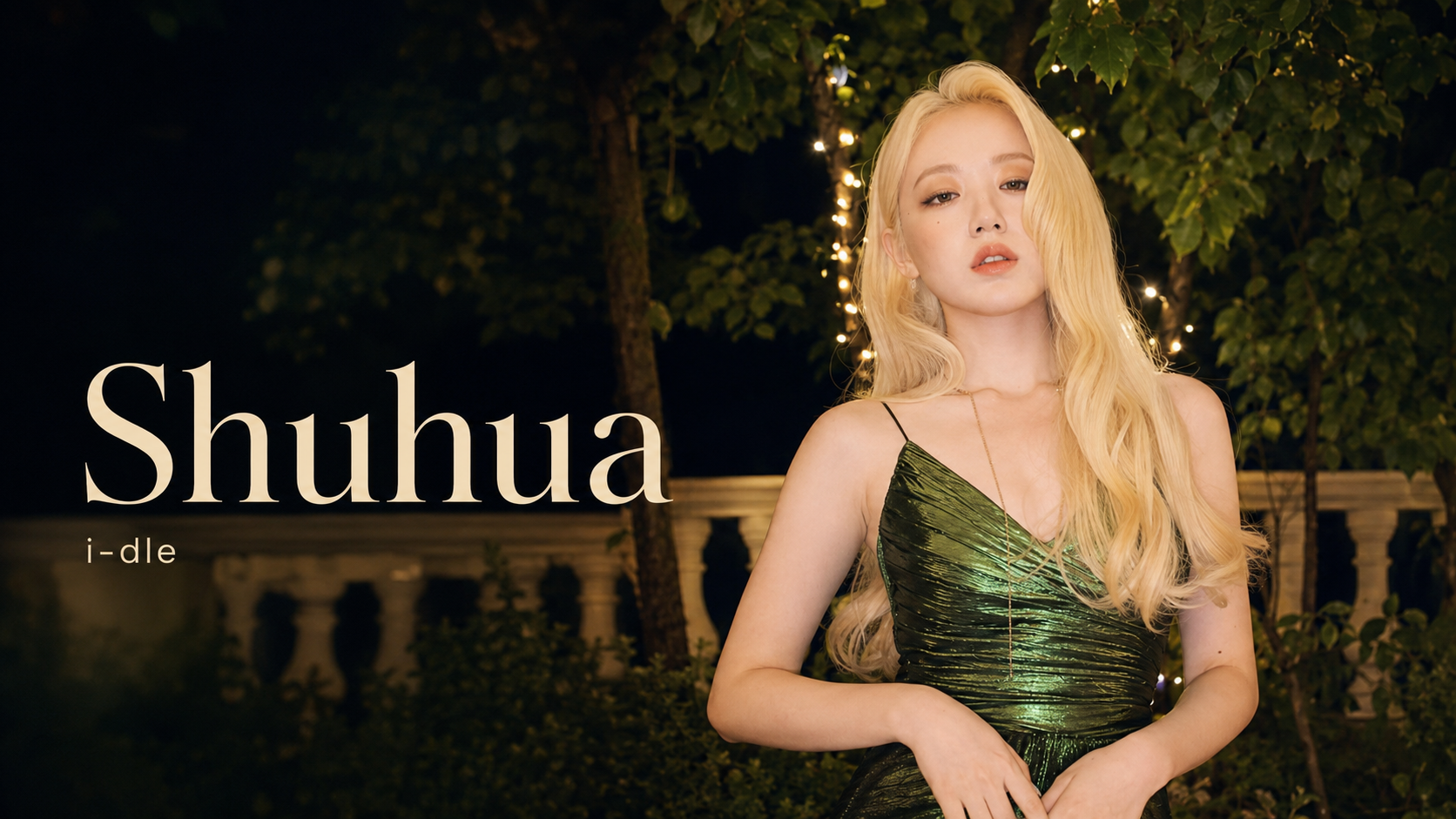 i-dle Shuhua 宣傳肖像,金色長髮女性穿綠色亮面服裝,站在樹木與燈串前,畫面標示 Shuhua、i-dle