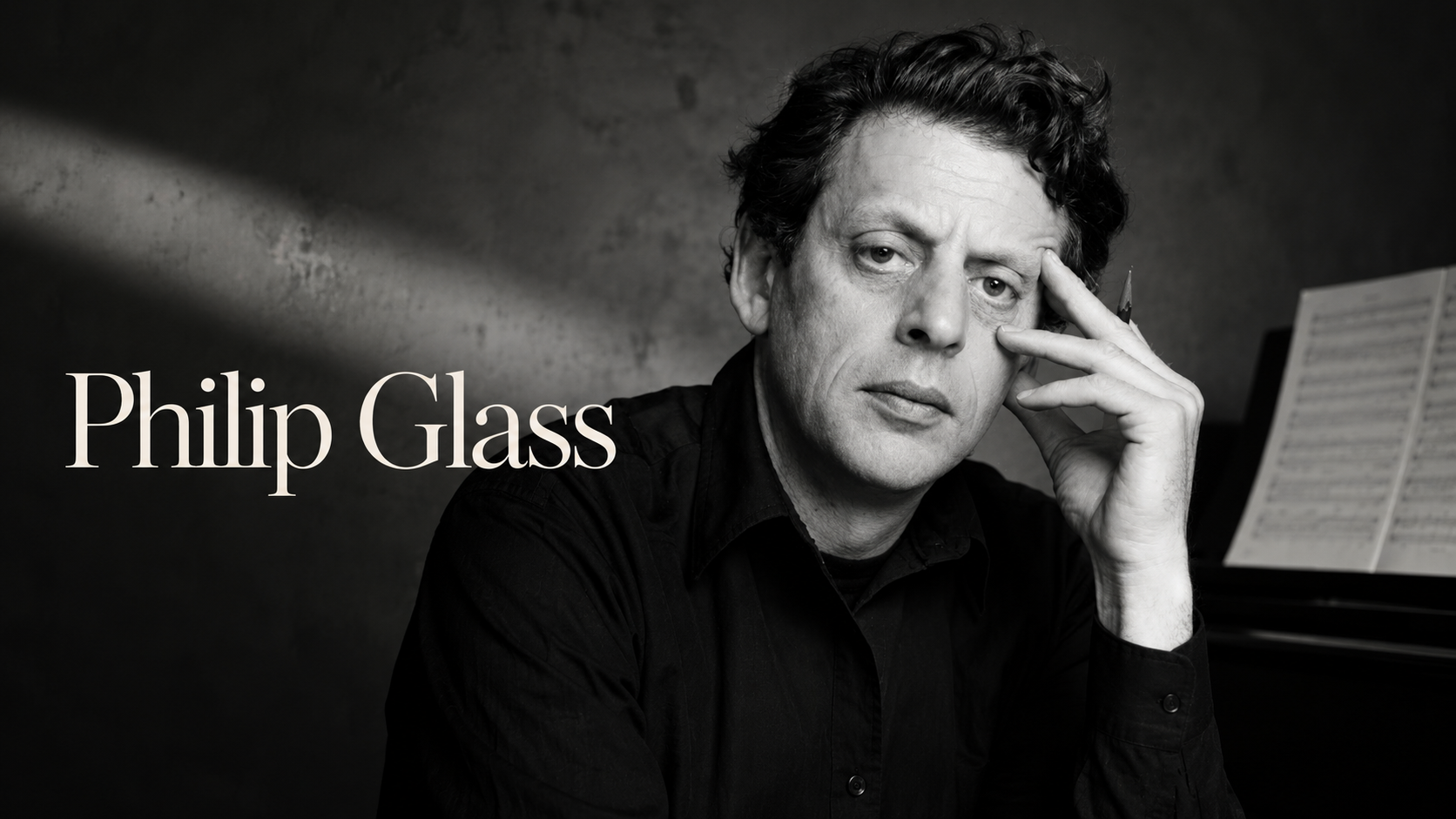 Philip Glass黑白肖像,身穿黑衣坐在鋼琴與樂譜旁,手扶額頭
