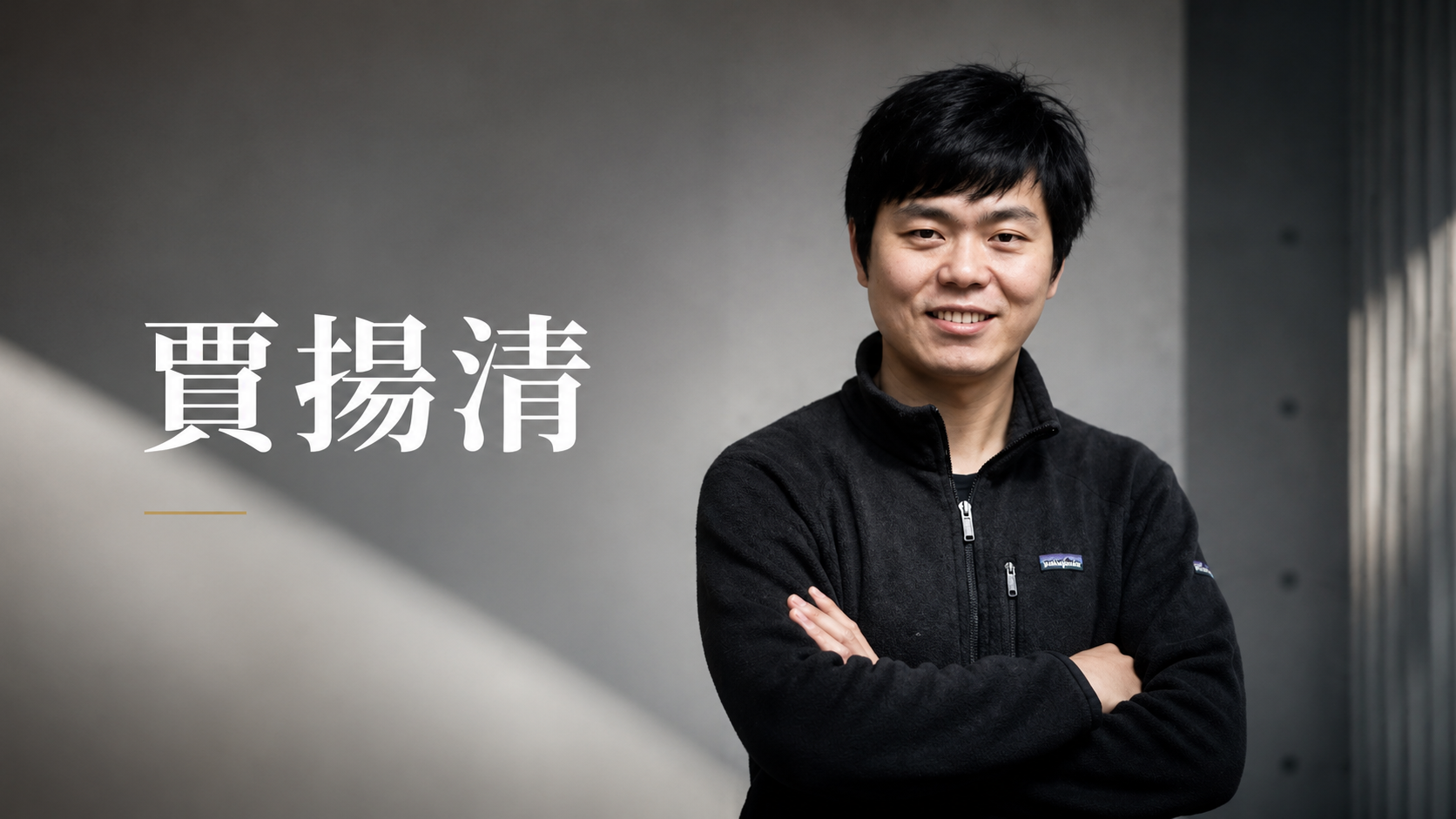 賈揚清肖像,穿黑色上衣、雙手交叉,站在灰色室內背景前。
